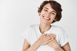Close up of happy smiling woman say thank you, holding hands on heart grateful, express gratitude, standing against white background.