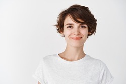 Head shot of beautiful caucasian woman with short haircut, smiling and looking confident, standing in t-shirt on white background.