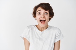 Portrait of surprised and amused caucasian woman, drop jaw and looking amazed at camera, white background.