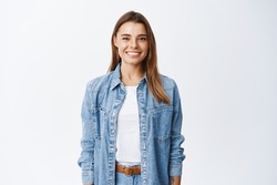 Young smiling blond girl with perfect teeth staring at camera, standing relaxed against white background in casual clothes, lifestyle and emotions concept