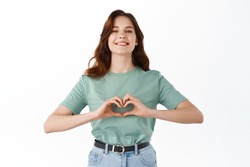 Beautiful girlfriend smiling and showing I love you hands heart gesture, like something nice, standing against white background