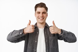 Close up portrait of happy smiling young man, boy shows thumbs up, nod approvingly, satisfied with choice, recommend something, praise or compliment, white background
