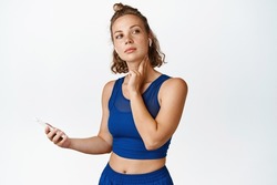 Young fitness woman checking pulse on her neck, using mobile app to track health vital signs during workout, sport exercises, white background.