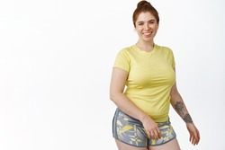 Portrait of smiling chubby redhead girl workout in gym, standing in fitness clothes, standing over white background