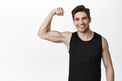 Workout and gym concept. Smiling handsome man showing his muscles after sport exercises, flexing biceps with pleased face, white background