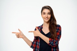 Tender girl dressed in plaid shirt smiling and pointing finger. Over white background.