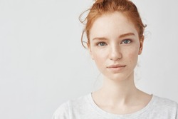 Close up portrait of young beautiful redhead girl in white shirt smiling looking at camera. Copy space. Isolated on white background.