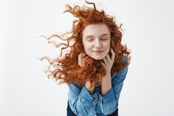 Attractive cheerful redhead girl with flying curly hair smiling laughing with closed eyes over white background.