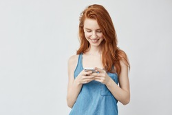 Happy beautiful redhead girl looking at phone and smiling.