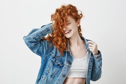 Happy beautiful girl smiling with closed eyes touching her red curly hair over white background.