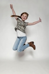 Young Girl in Jeans and Camo Shirt Jumping for Joy against a White Background