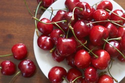 Fresh red cherries fruit on plate on wooden background close up. High quality photo