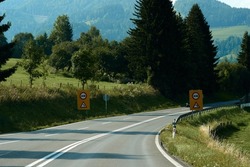 Asphalt road through green summer field and forest, mountains landscape, road signs. High quality photo