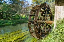 Water mill wheel on river on sunny day. Sustainable energy and water power traditional machinery