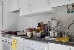Kitchen of a house with a dirty countertop full of empty dishes and kitchen utensils for scrubbing and storage jars