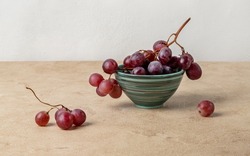 Still life with red grapes lying in a ceramic bowl. Beige textured background, horizontal orientation.