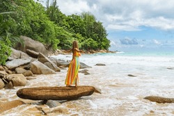 A photo of a young woman expressing joy and wonder atop a log on the small, secluded Nai Thon beach on the island of Phuket, Thailand. 