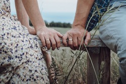 Portrait photo session of bride and groom on the field of village in country style. Light tone wedding on nature among dry grass. Man and woman are wear country clothes sitting on bench cute talking.