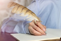 Hands close up. A woman with a French manicure in a blue shirt writes with a feather in a notebook. Business woman  making notes on paper. 