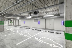 Empty public underground parking lot or garage interior with concrete stripe painted columns and signs. Electric car charging place.