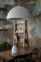 Stylish interior design of dining room in forest mood with solid oak table, shelf and green chairs, concrete vase, elegant cement accessories, recycled paper lamp shade and clay wall in earth tones