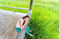 A young Thai woman sits on a squat with her eyes closed, her head tilted to the floor, listening to the sound of nature. located in the farmer's fields It is a beautiful natural rice growing season.