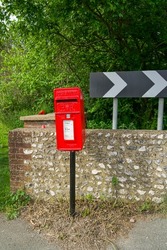 A bright red metal mailbox for sending paper letters stands along the road. An old-style mailbox.	