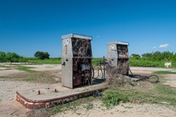 Abandoned Gas Station Pumps in Empty parking lot surrounded by blue sky and bushes