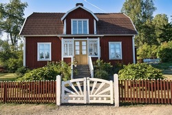 Swedish red and white traditional house in Smalland, White fence green garden blue sky. Childhood memories from the vacations in Sweden. Nature photo from Scandinavian landscape.