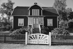 Swedish in black and white shot. tratitional house in Smalland, White fence green garden blue sky. Childhood memories from the vacations in Sweden. Nature photo from Scandinavian landscape.