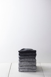 stack of folded t-shirt of black colors and gray variation (monochrome) on white wood background, copy space
