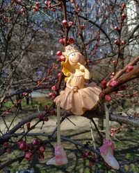 The fairy figurine sits on the trunk of a blossoming tree. Ceramic decorative hanging fairy princess figurine. A fabulous story against the backdrop of spring nature.