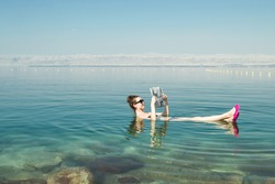 Photo of the Girl reading newspaper floating on surface Dead Sea enjoy summer sun and vacation. Recreation tourism, healthy lifestyle, free time concept