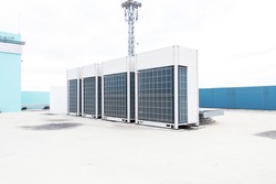 Big air conditioner compressor source heat pumps on the wall outdoor on the roof top of the building. It is used in large industrial buildings for cooling. with sky and spotlights in the background.