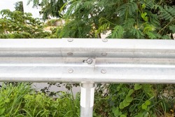 Bridge railing nut, pole. Bridge railing, bolts attached to posts. Roadside bridge fences are made steel, aluminum do not rust. Safety concept. with green trees in the background.