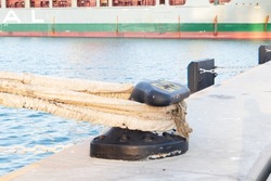 Sturdy metal mooring bollard at pier big lack with a rope attached.  Used for large cargo berth use ropes to keep ships from moving. Single mooring device with coiled ropes keeps ship on dock.
