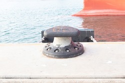 Sturdy metal mooring bollard at pier big lack attached to concrete. single mooring device with coiled ropes keeps ship on dock. Used for large cargo berth use ropes to keep ships from moving. 