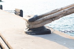 Sturdy metal mooring bollard at pier big lack installed on concrete with a rope attached.  Used for large cargo berth use ropes to keep ships from moving. Single mooring device with coiled ropes.