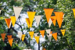 white, yellow and orange triangle flags hang on white rope in garden view. concept : fun party.