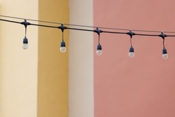 string wired bulbs decoration outdoor of building. garland of a light bulbs with the yellow and pink concrete wall background.