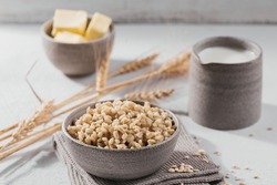 Bowl of cooked peeled barley grains porridge with ears of wheat on white background. Cooking Healthy and diet food concept.