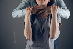 a man strangles a girl from behind on a dark background