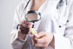 the doctor looks at the pills with a magnifying glass. drug search concept on gray background