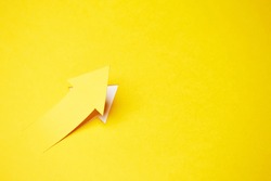 Right-up arrow cutted from solid sheet of yellow paper and curved up of one side with white paper underlay showing growth of stock market or up direction