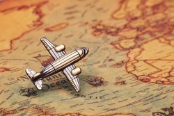 Small toy airplane vintage classic old school style model hovering in take off mode above the ancient antique old-fashioned style world map direct flight from left to up right side in the 45 degree