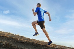 man athlete runner running uphill in background blue sky