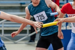 men relay race baton passing in summer athletics championship, close-up of athletes hands on background of runners