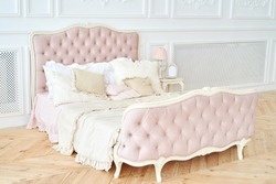 Big comfortable royal bed with pillows in elegant bedroom interior, copy space. Honeymoon suite, free space. Female bedroom in pink and white colors. Luxury bed in romantic style. Boudoir