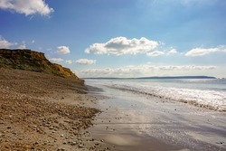 Coastal view across beach with rugged cliff. Walk on the beach in England. Calm day on quiet beach 