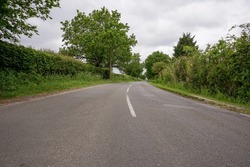view along quiet country lane. Empty road with trees and hedges at the sides. Middle of a road. Road trip in rural England.